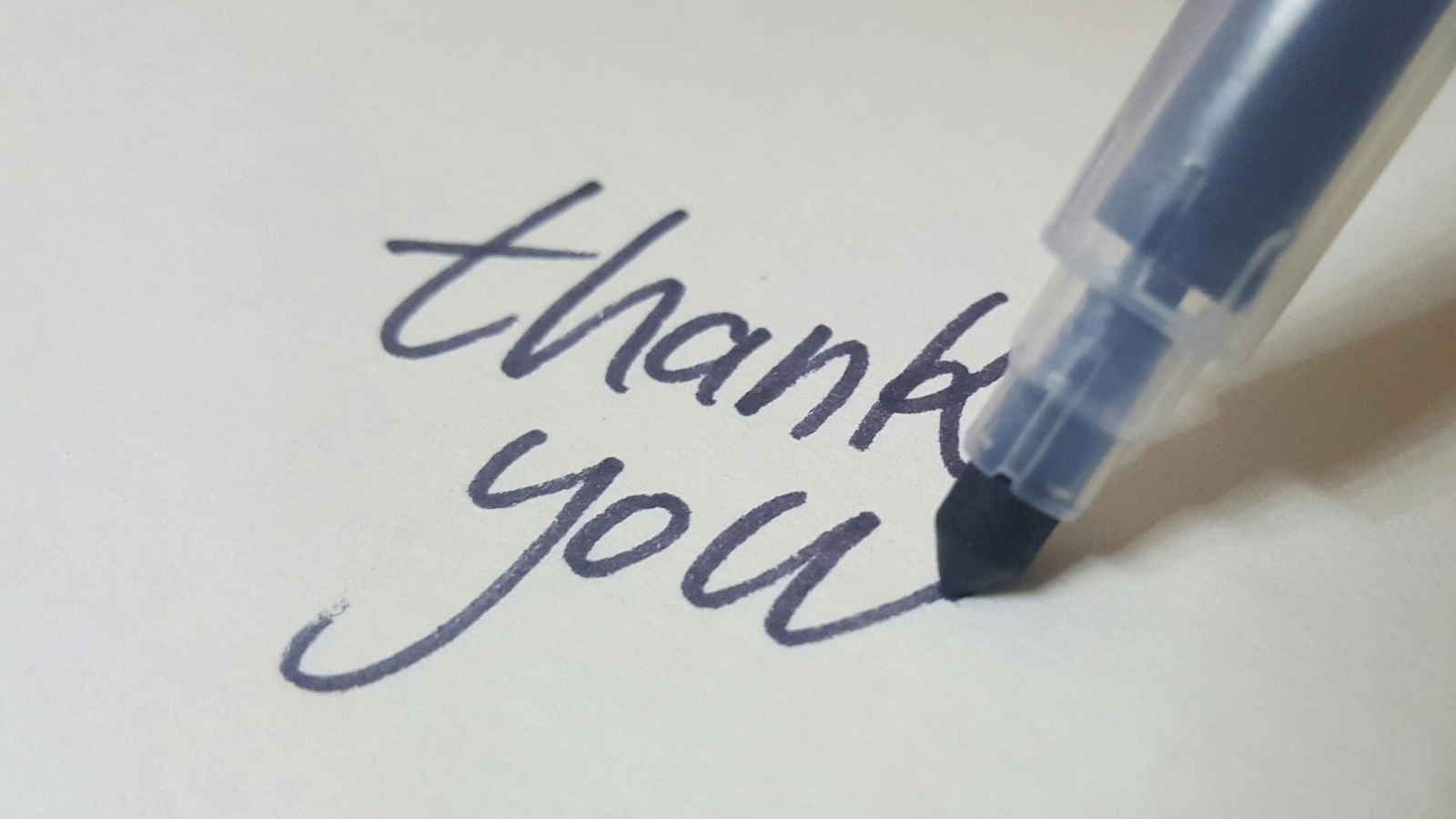 A dark blue felt tip pen writing 'thank you' on white paper
